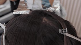 Close-up of the process of highlighting the long brown hair of a girl. The hairdresser prepares the strong beautiful hair of the girl for highlighting, combing the hair, wrapping wet hair in foil