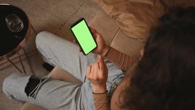Closeup of woman holding smartphone chromakey green screen watching content sitting on couch at home. Gadgets people concept.
