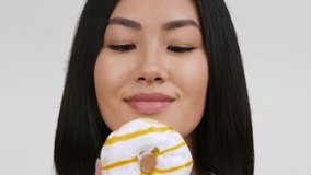 Cheerful Korean Lady Posing With Donut Smiling To Camera Standing Over White Background. Portrait Of Pretty Asian Female WIth Doughnut In Studio. Sugary Food, Sweet Tooth Concept