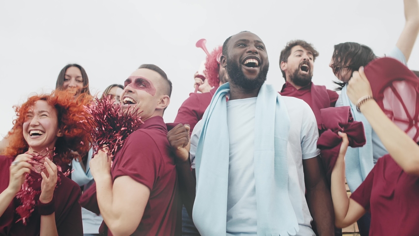 Happy multi ethnic sport supporters in red and blue having fun during football league world olympic game and celebrating a goal and victory Royalty-Free Stock Footage #1074319049