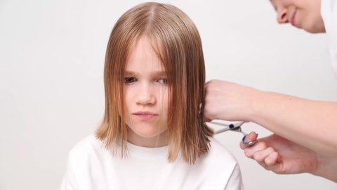 woman does the haircut of a yawning girl on a white background. Mommy is a hairdresser. saving money at a beauty salon. shampoos and cosmetics for children's hair.