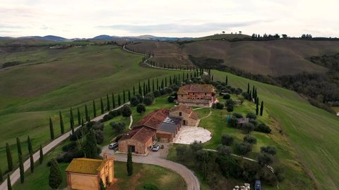 Tuscany countryside aerial shot with drone at sunset time - farmhouse, hills fields, vineyards, cypress trees along white road