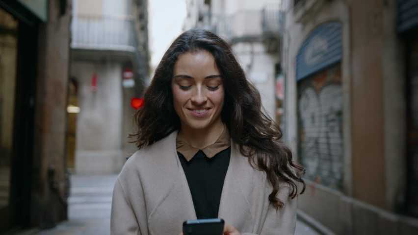 Young attractive brunette confidently walking narrow city streets and using smartphone to communicate or chat with her friends. Modern technology usability concept. Slow motion cinematic shot Royalty-Free Stock Footage #1074328415