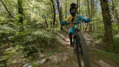 Aerial shot mtb biker athlete riding on hilly terrain at summer forest park with green grass trees. Sportsman rider on downhill bike almost crashed into fpv sport drone mtb woodland extreme activity