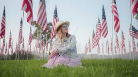 Slow motion woman sitting on green grass in urban park and looking on the American flags. Patriotic 4K footage Independence day, 4th of July, Labor day celebration concept. Remembering September 11th - Powered by Shutterstock - Get 15% off with code: PIKWIZARD15