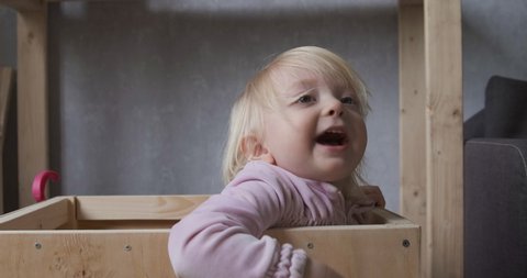 Small child is hiding in closet, playing hide and seek with his parents. Cute blonde girl jumps out of hiding and laughs.