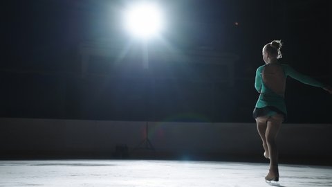 The girl skater performs a jump with the rotation of a triple toe loop in a counter light on an ice cat. Slow-motion jump in figure skating
