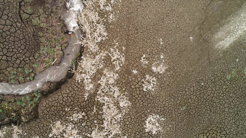 Aerial view of a dry lake bottom with deeply cracked soil and a small water spring. Video. Unusual texture with many cracks in the ground, concept of weather change and global warming.