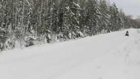 Winter snowy landscape with road and snowmobile riding along spruce tree forest. Clip. Concept of winter sports activities and active lifestyle.