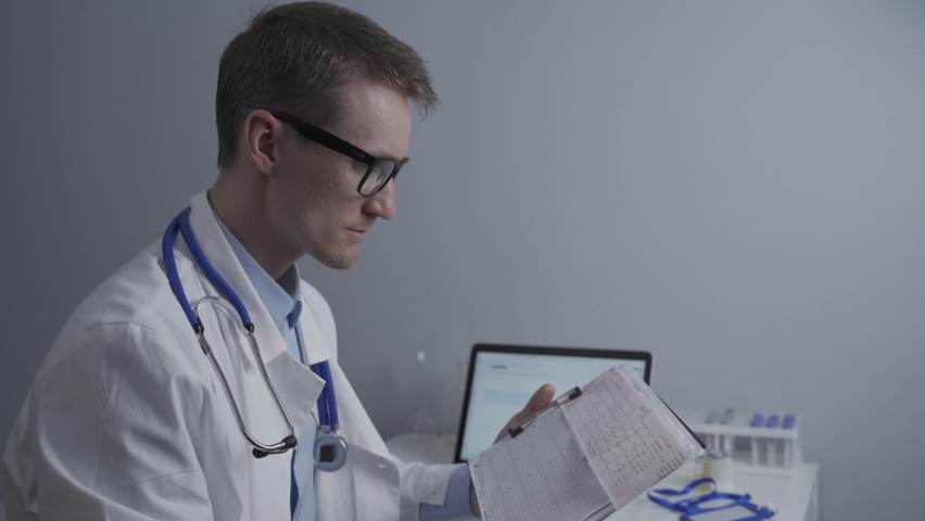 Cardiologist reading an ECG print-out. Doctor analyzing electrocardiogram. Practitioner examine patient test results. Medical and healthcare concept. Physician looking at cardiogram at medical office Royalty-Free Stock Footage #1074344957