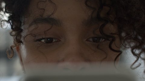 Extreme close-up of black african american girl texting or reading on her handheld mobile cell phone with focus on eyes.