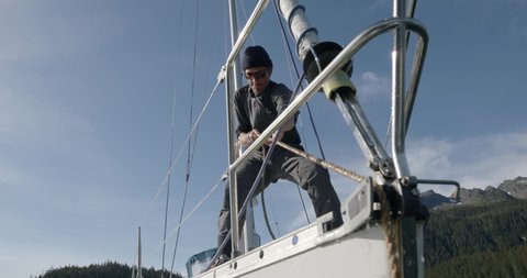 Slow Motion of Male at Bow of Sailing Boat Pulling Rope and Chain With Anchor on Sunny Day at Alaskan Coastline