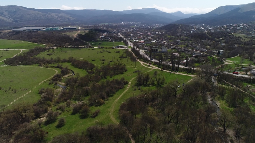 Charming small town located in the green valley, ecological place for living. Shot. Picturesque natural landscape with meadows, green trees and mountains far in the distance.