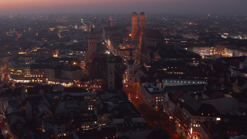 Approaching City Center of Munich Big City in Germany at Night from Aerial Drone perspective, City lights glowing on the street with view on Marienplatz and Frauenkirche