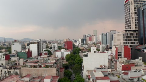 Rooftop view of low residential houses neighbors with tall office buildings. Low forward flying drone camera over city downtown. Mexico city, Mexico.