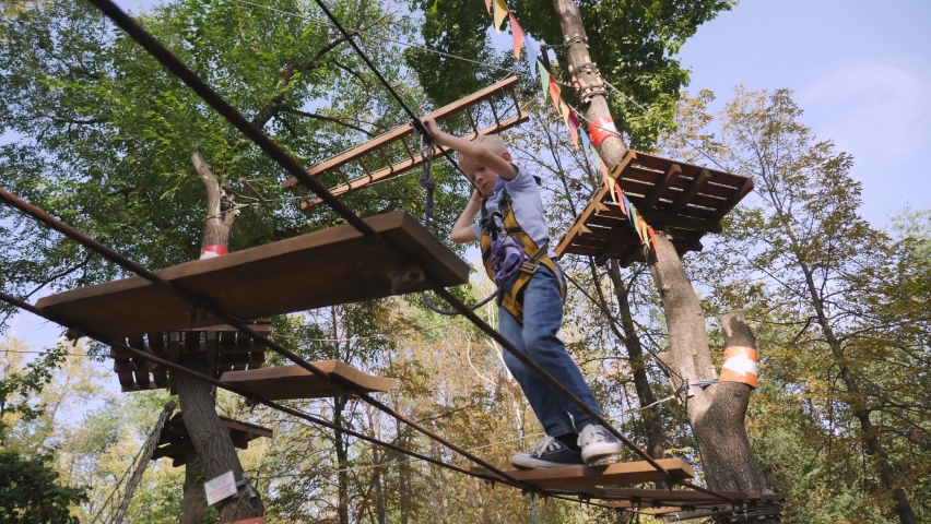 Happy school boy enjoying activity in a climbing adventure park on summer day.