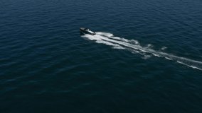 Dark blue big boat fast movement on dark blue water aerial view. Horizontal flight over a dark blue speed boat in motion. High-speed motor boat with a man moving on the water.