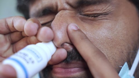 Extreme close up of Young man with medical face mask inhales coronavirus covid-19 nasal vaccination spray to protect from virus infection.
