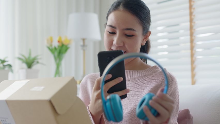 Young asia people happy teen girl smile unbox open gift new headphone buy order from online store shop take photo shoot camera show post social media app blog vlog share sit relax at home sofa couch. | Shutterstock HD Video #1074362918