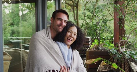 Smiling mixed race couple wrapped in sheets embracing each other in the balcony at vacation home. couple honeymoon and vacation concept