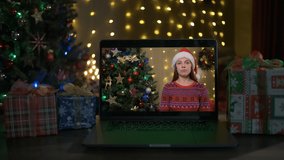 Smiling woman with santa hat on a videocall, she is happy and wishing a merry Christmas online, Christmas tree and decorated room interior in the background