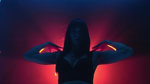Portrait of young woman moves her arms in studio - modern vogue. Lady performing dance on colorful spotlight background. Concept of sexual dancing with neon backlight.