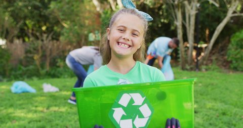 Smiling caucasian daughter outdoors holding recycling crate, collecting plastic waste with parents. eco conservation volunteers doing countryside clean-up.