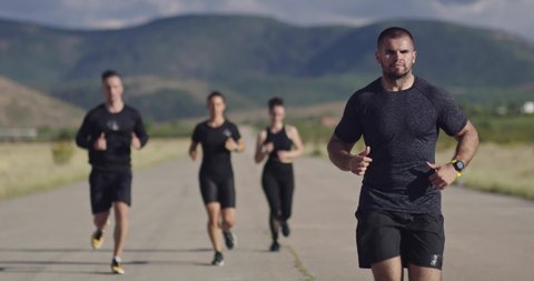 Multiethnic group of athletes running together on a panoramic countryside road. Diverse Team of joggers on morning training. 