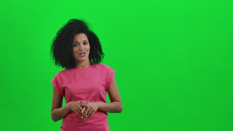 Portrait of young female African American is reporting and telling a lot of interesting information. Black woman with curly hair poses on green screen in studio. Close up. Slow motion ready 59.97fps.