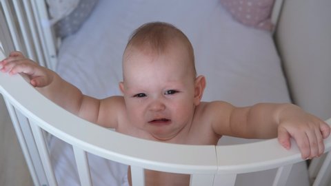 Close-up of a small child standing in a crib. The toddler does not want to sleep in the bed.