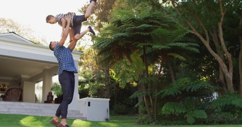 Happy caucasian son running and jumping into the arms of father in sunny garden. happy family spending free time together at home.