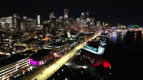 Cinematic 4K drone, after sunset, night video of downtown Seattle, Washington, Alaskan way waterfront with illuminated streets and offices looking from Elliott Bay Seattle Harbor during blue hour