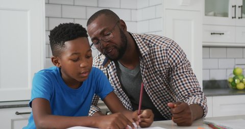 African american father sitting at kitchen table helping son with school work. family spending time together at home.