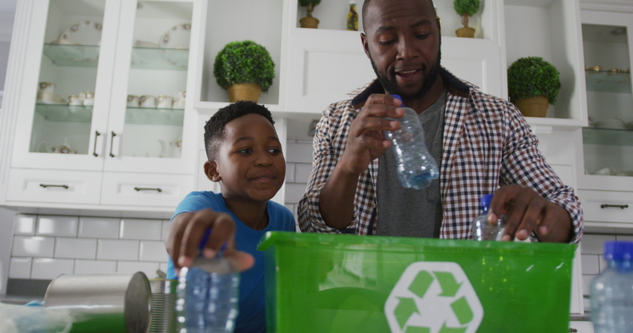 Happy african american father and son standing in kitchen putting plastic rubbish in recycling box. family spending time together at home. | Shutterstock HD Video #1074385226