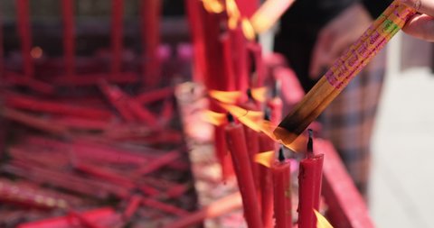 close up hand burning incense sticks on red candle fire in temple. Asian Buddhism culture concept  