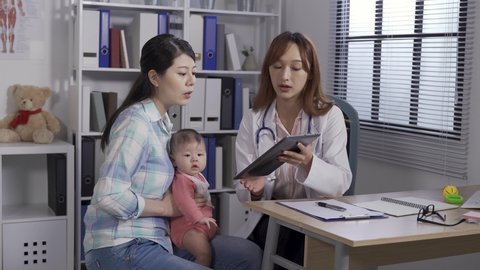 korean mother holding baby pointing to pad screen and making inquiries during her visit in a well-child clinic.