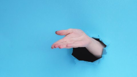 Pay me. Hurry up. Woman hand demanding money with rude gesture from breakthrough paper hole isolated on blue torn background with empty space. Alimony debt.
