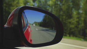Red automobile in motion. View in the rear view side mirror of a auto, driving a red car along the track
