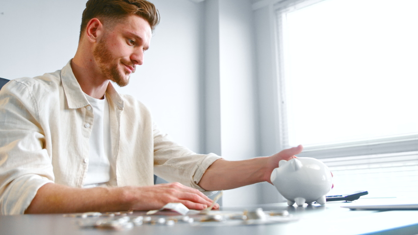Bearded company worker shakes and hits white piggy bank