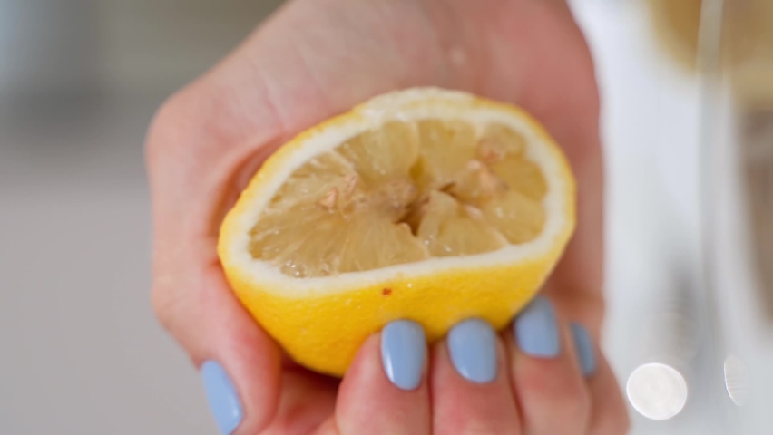 Hand squeezing lemon juice out of lemon, very close-up vertical shot. slow motion. fresh lemon with seeds in a woman's hand
