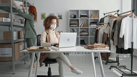 quarantine purchases, young female companions in medical masks work in online clothing store and arrange dispatches with goods for delivery to customers sitting on stock boutique