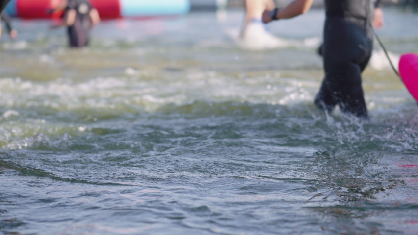 Slow motion people wearing wetsuits walking in water in slow motion, focus on waves on foreground. Partial view of contestants of aquatic competition. Concept of sport