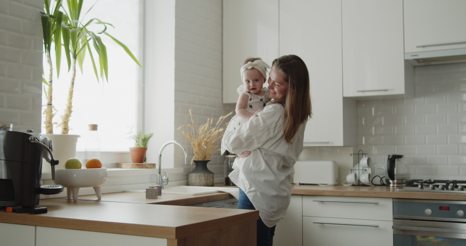 Mother and daughter spend time at home together. Young mom dances with her adorable little child in the kitchen holding her in arms. Woman and her baby have fun together. Royalty-Free Stock Footage #1074399038