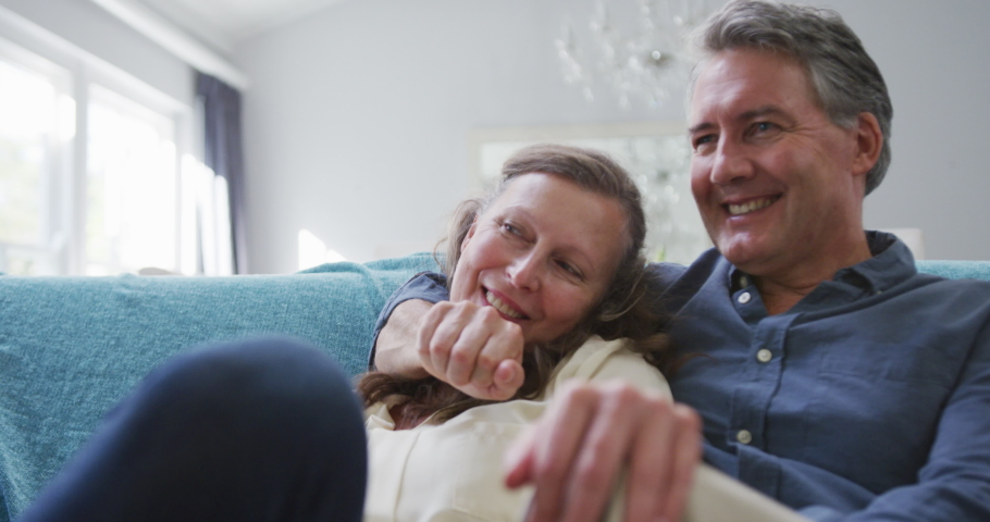 Happy senior caucasian couple sitting in living room watching tv and talking. retirement lifestyle together at home.