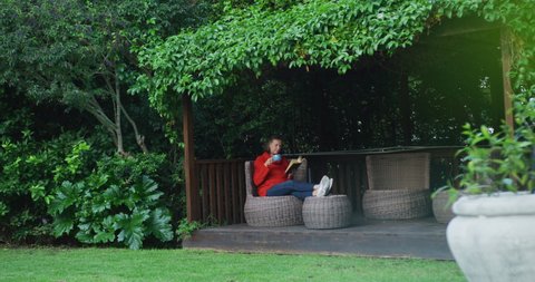 Senior caucasian woman relaxing in garden, sitting with feet up, drinking coffee and reading book. retirement lifestyle at home alone.