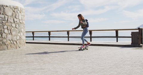 Happy mixed race woman skateboarding on sunny promenade by the sea. healthy living, off the grid and close to nature.