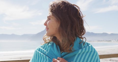 Portrait of happy mixed race woman standing by the sea with blanket over shoulders smiling. healthy living, off the grid and close to nature.
