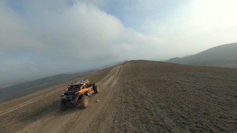 Shooting from sport fpv drone extreme orange buggy car racing speed jump riding on hilly terrain at natural valley. Aerial shot auto transport rally fast skill motion adventure road sand dune desert