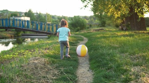 summer, vacation, nature, happy family, childhood - one small toddler preschool child baby kid girl runing by footpath play with big inflatable ball catch in park on grass at sunset outside fresh air