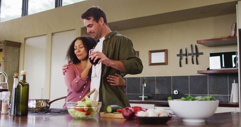 Happy diverse couple preparing a meal together in kitchen, drinking wine and embracing. spending free time together at home.